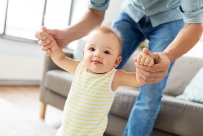father helping baby daughter with walking at home
