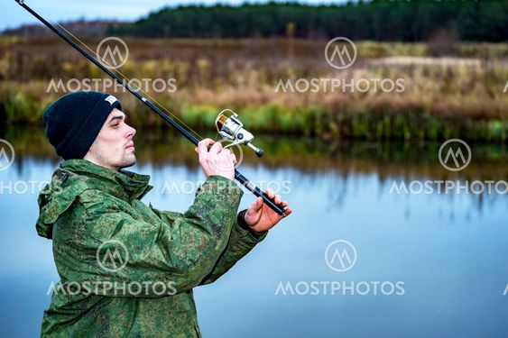 Male angler catches on a spinning fish in cold water in...
