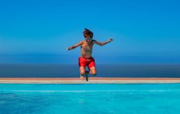 Cute tanned teen in goggles jump carefree at a seaside pool