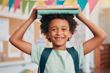 Boy, smile and books on head in classroom, portrait and...