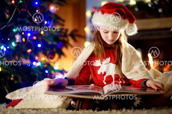 Happy little girl reading a story book by a fireplace in...