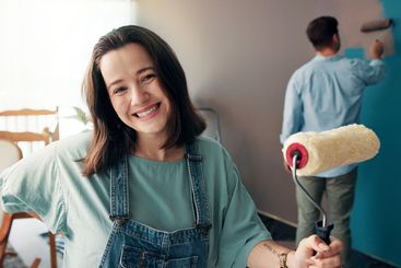Happy woman, nursery and paint brush in home for...