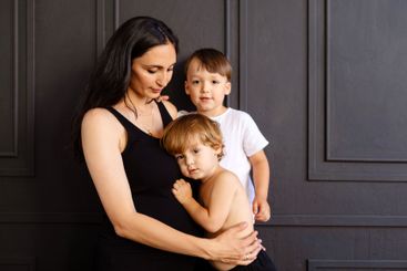 A young pregnant woman hugs her little children at home....