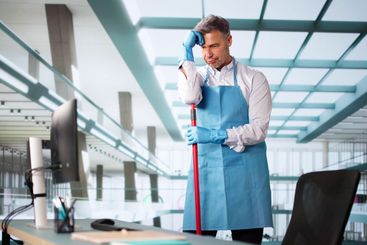 Young Male Janitor Cleaning Computer With Rag
