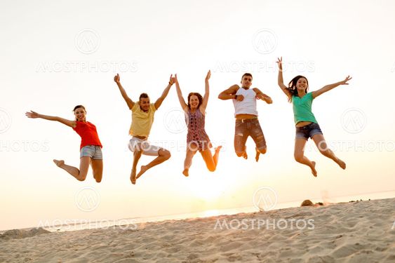smiling friends dancing and jumping on beach