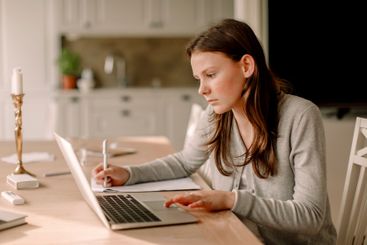 Teenage girl using laptop while studying at dining table...