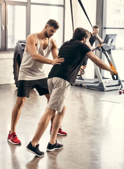 side view of trainer helping sportsman exercising with...