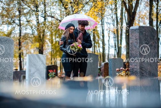 Couple mourning a deceased loved one on cemetery in fall