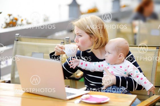 Tired young mother holding 6-month daughter and drinking...