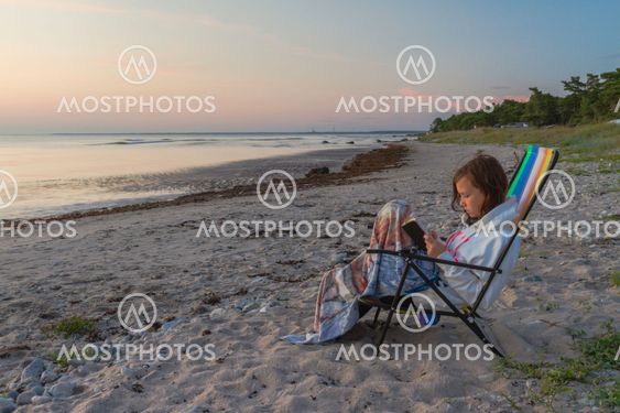 White teenager sitting on a beach and reading