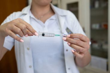 A focused nurse in a white lab coat carefully prepares a...