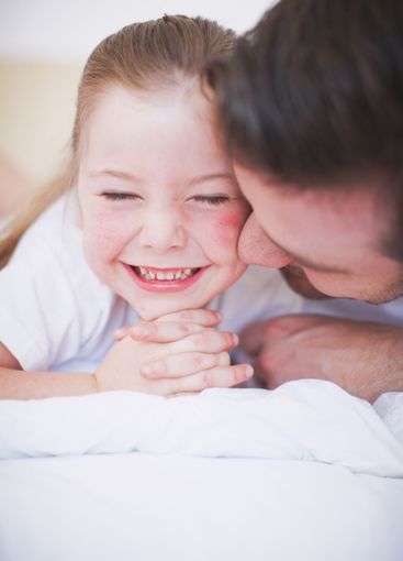 Daughter, dad and playful kiss in home, fun and love for...