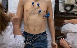 A female doctor performs an ECG on a young man in a...