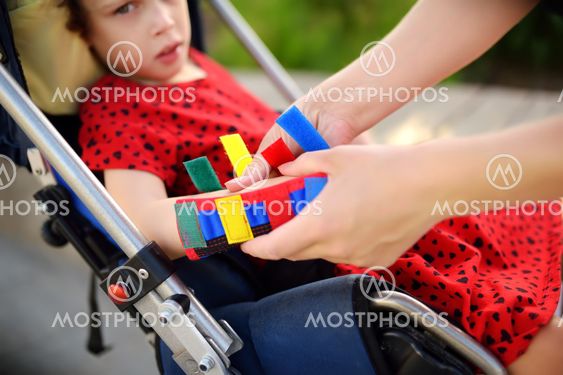 Mother puts orthosis on her daughter arms. Disabled girl...