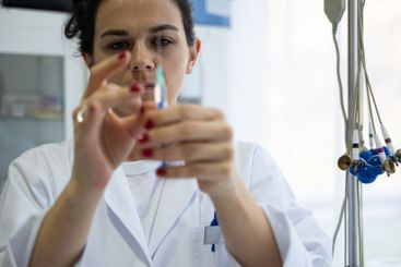 A focused nurse in a white lab coat carefully prepares a...