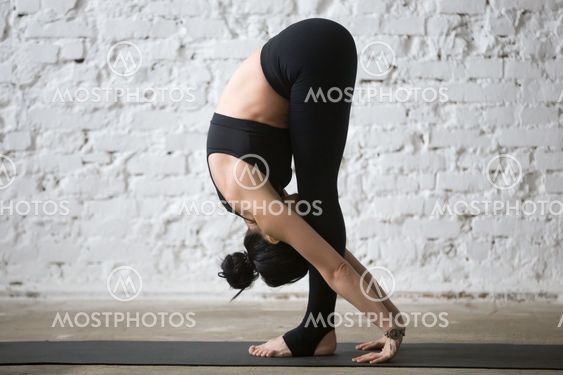 Young yogi attractive woman in uttanasana pose, white loft backg