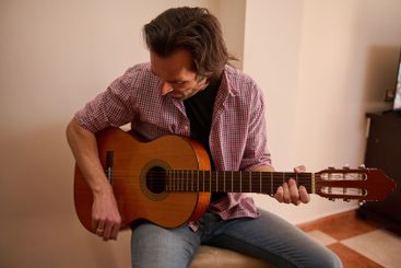 Man playing acoustic guitar indoors wearing a casual...