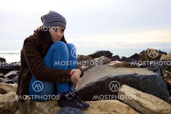 Sad young woman sitting in front of the ocean in the winter