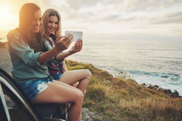 Sea, women and selfie at sunset for road trip and...
