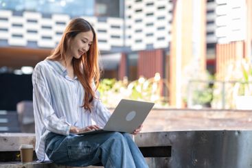 Woman is sitting on a bench and using a laptop