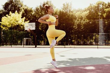 Sporty black woman in yellow sportswear jumping and running