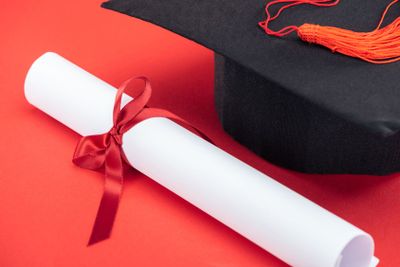 Academic cap with tassel and diploma with ribbon on red...