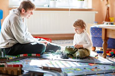 Father and son playing with racing cars on racetrack,...