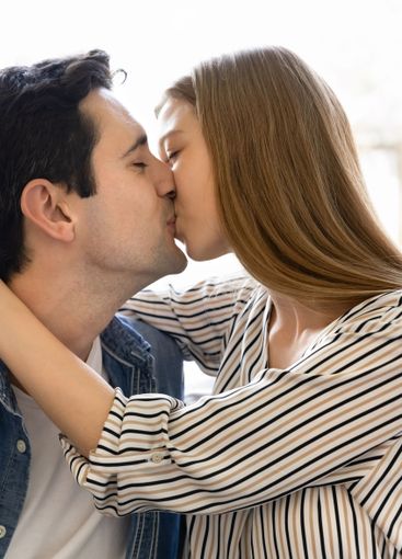 Happy young Hispanic couple in love kissing on lips indoors
