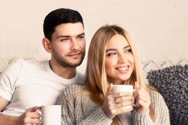Newlyweds with hot tea cuddling on sofa indoors