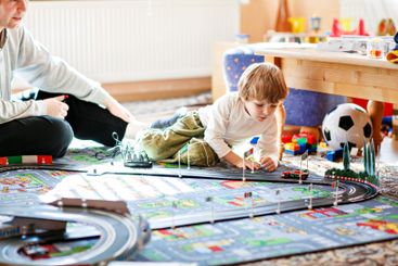 Father and son playing with racing cars on racetrack,...