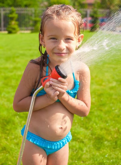 Happy adorable little girl smiling and pouring water from a hose