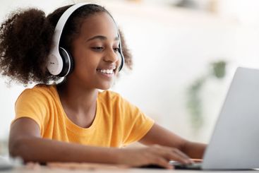 Cheerful black girl studying online, using laptop and...