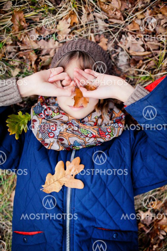 Girl lies on autumn leaves and covers her face