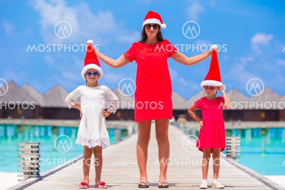 Happy mother and little girls in Santa hat near water villa on summer vacation