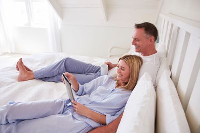 Couple Lying In Bed Looking At Digital Tablet Together