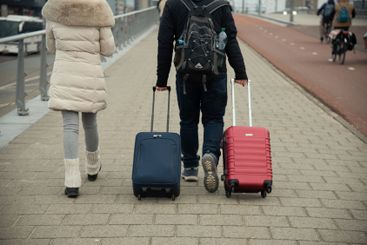 Travelers walking on a city sidewalk pulling luggage.