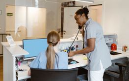 Side view of female healthcare professional attending call while standing next to receptionist at hospital