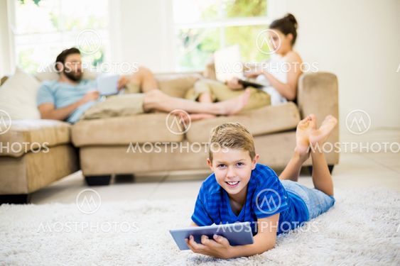 Portrait of boy lying on rug and using digital tablet