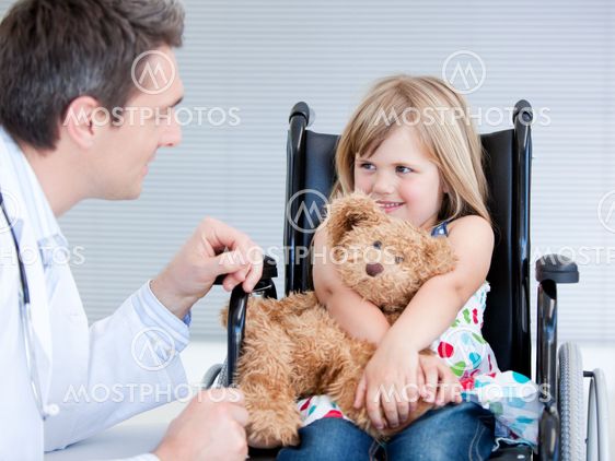 Smiling little girl sitting on the wheelchair lokking at the doctor