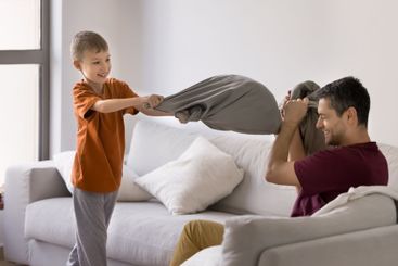 Little boy holding pillow fighting with father at home