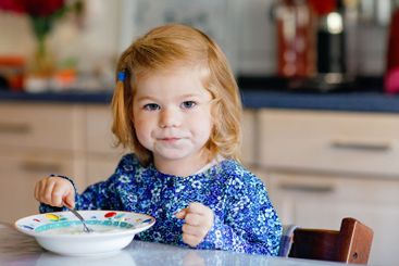 Adorable toddler girl eating healthy cereal with milk...