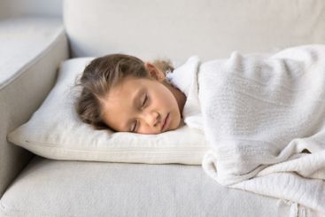 Little girl falling asleep on white sofa, closeup