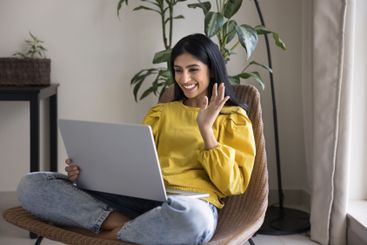 Smiling woman start videocall using laptop seated on...