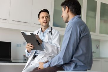 Caring young male doctor meeting with patient in clinic...