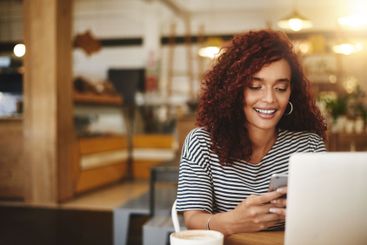 Woman, laptop and phone with remote work at cafe, smile...