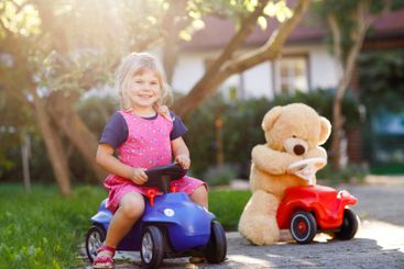 Little adorable toddler girl driving toy car and having...