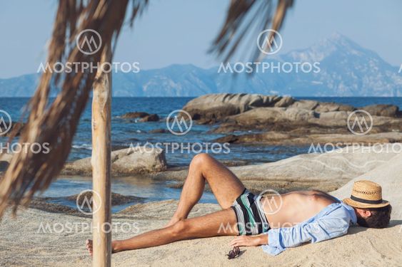 Young man relaxing on the beach, sunbathing on a rock...