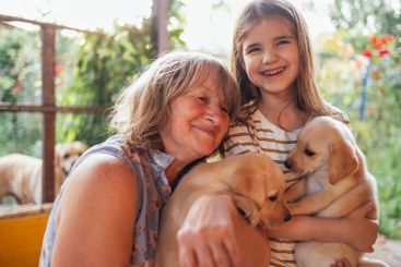 Mature woman hugs puppies and her granddaughter. Smiling...