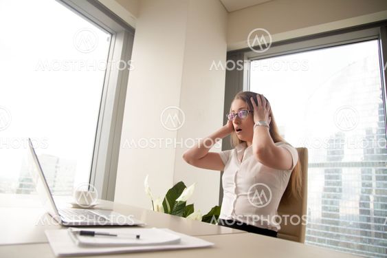 Surprised businesswoman sitting with head in hands