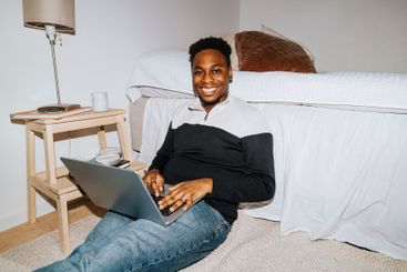 Portrait of smiling male student with laptop sitting by...